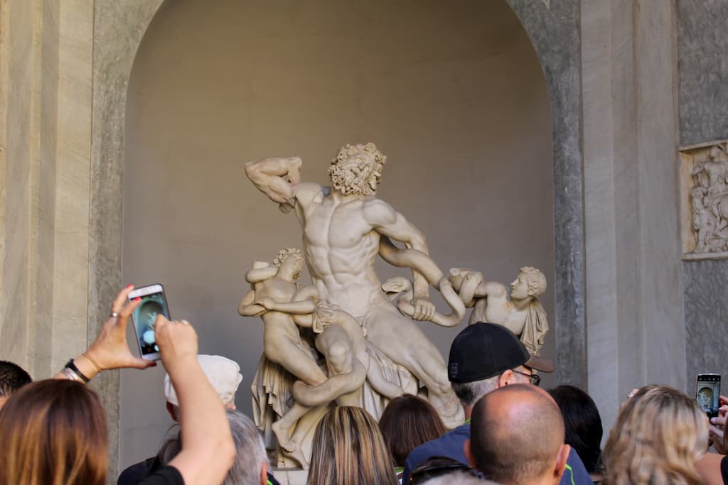 People looking at a stone statue of a man and his two sons struggling against sea snakes