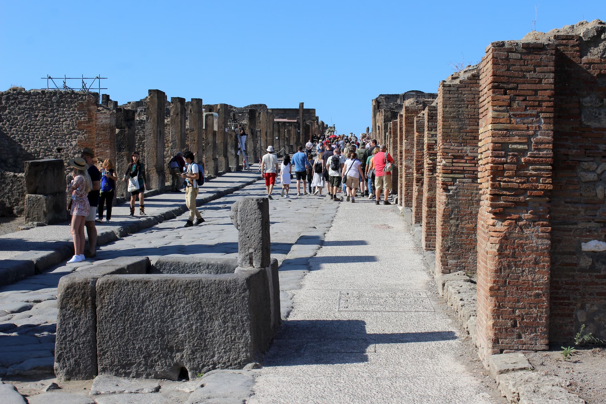 ancient, stone street with the walls of old buildings and tourists walking