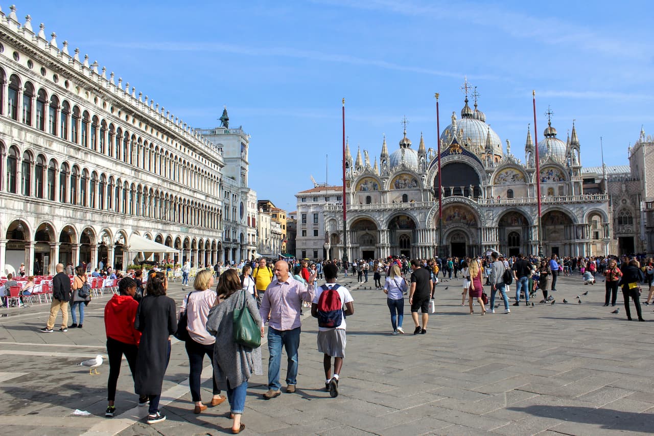 People walking in old city square with ornate church in the background.