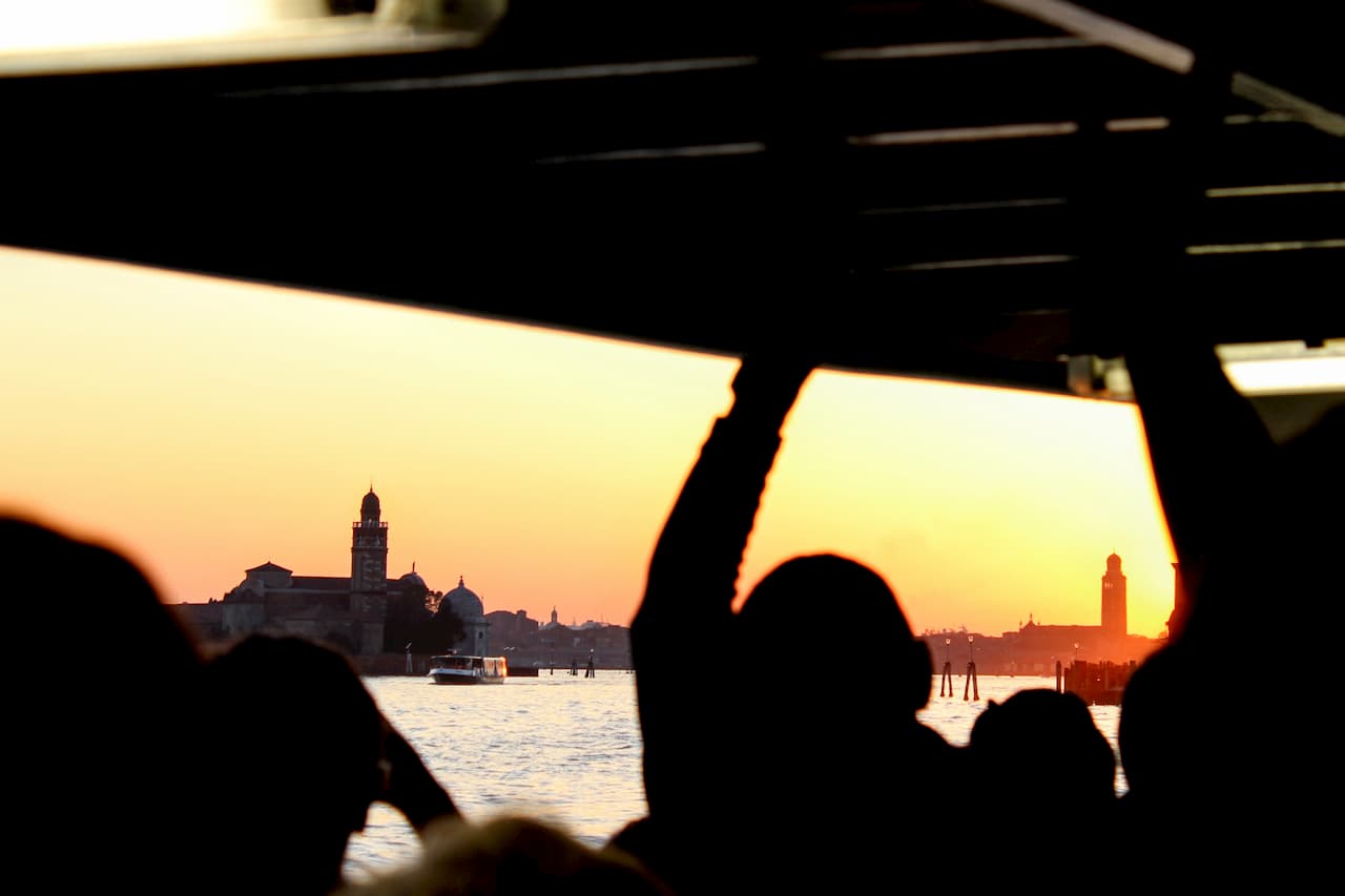 Silhouette of people inside a boat looking out at a city at sunset.