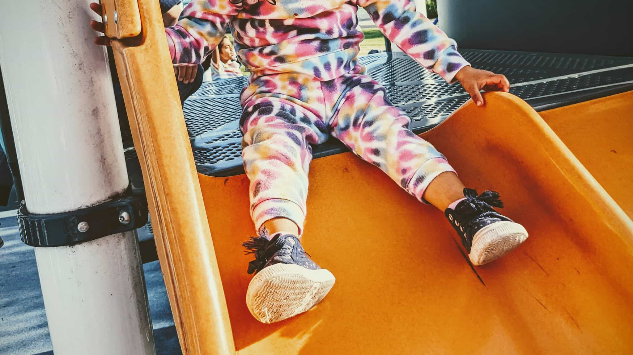 closeup of small child at top of a playground slide, face not pictured.