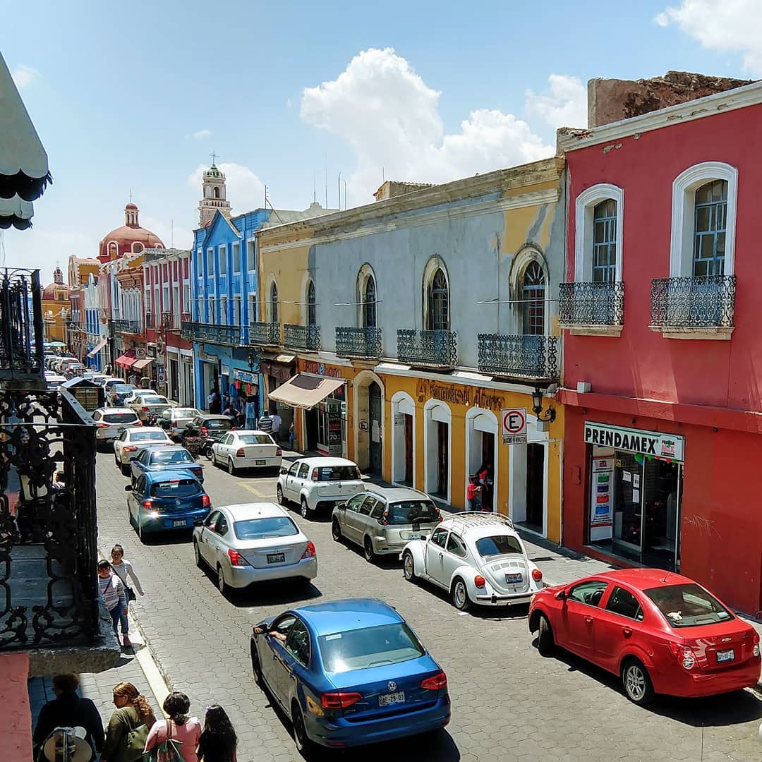 A line of connected buildings with colorful facades on a street with traffic.