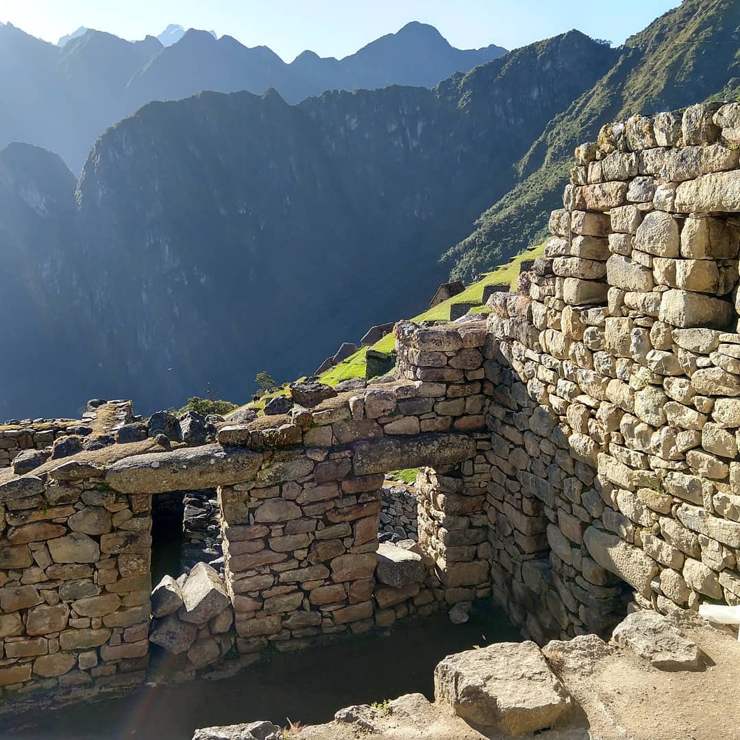 Parts of a two story high stone building wall with large windows. Green hills are visible behind.