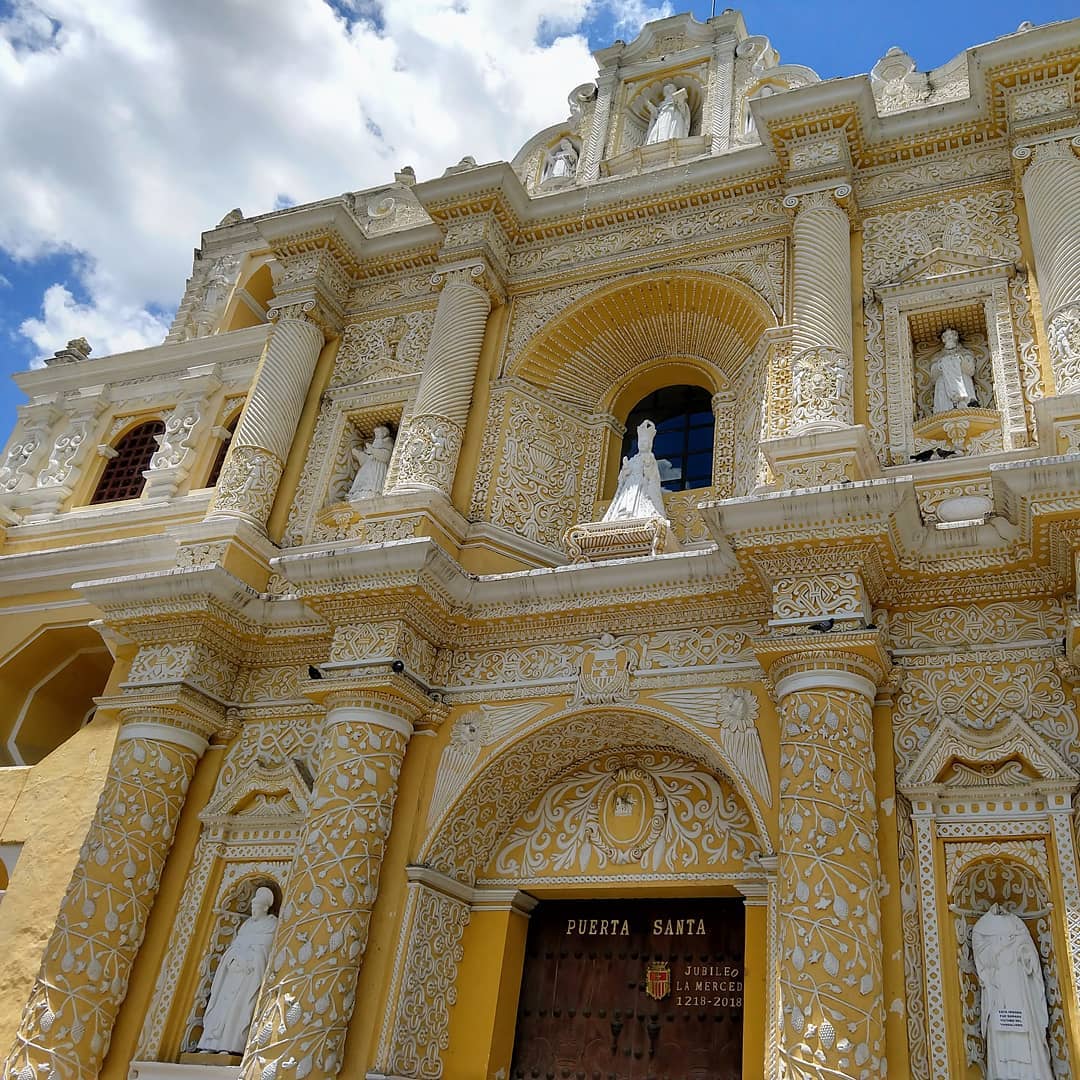 Face of a yellow church with white carvings all over the surface. White statues stand and look out from altars.