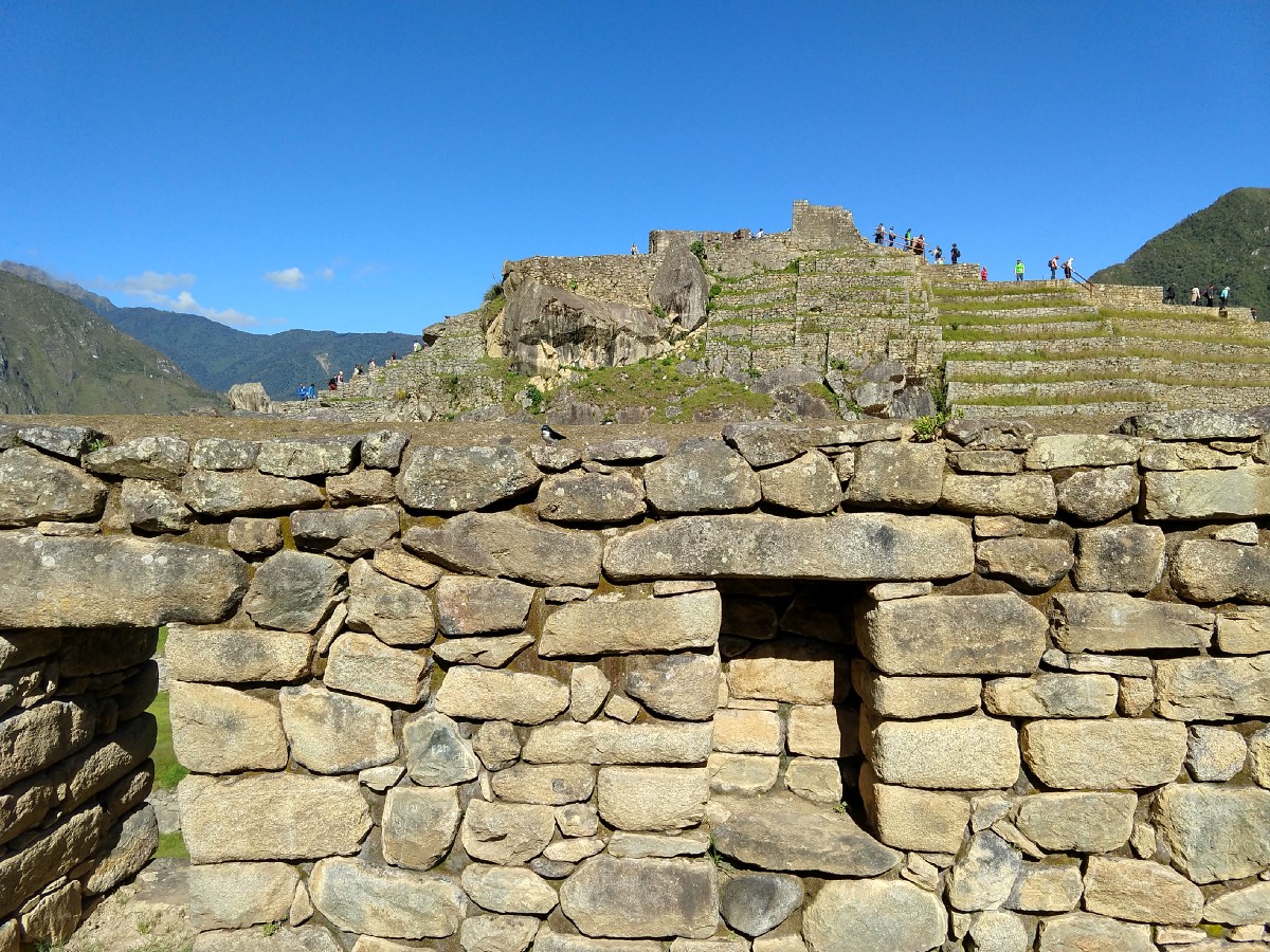 Stone wall of house topped with a blue and white bird, more stone structures in background