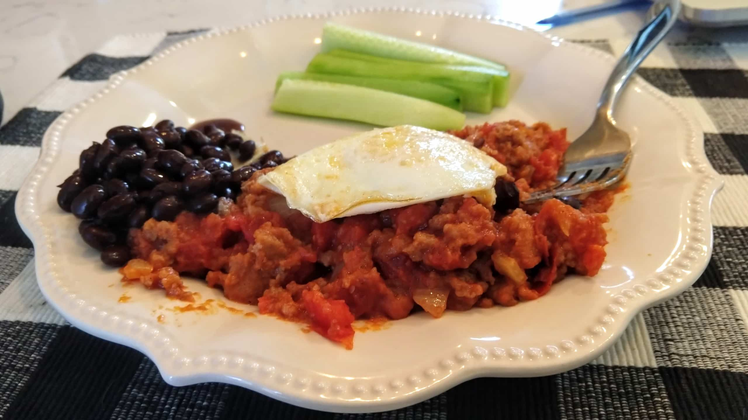 Dish with sauce and bread bits served with egg, beans, and cucumber.