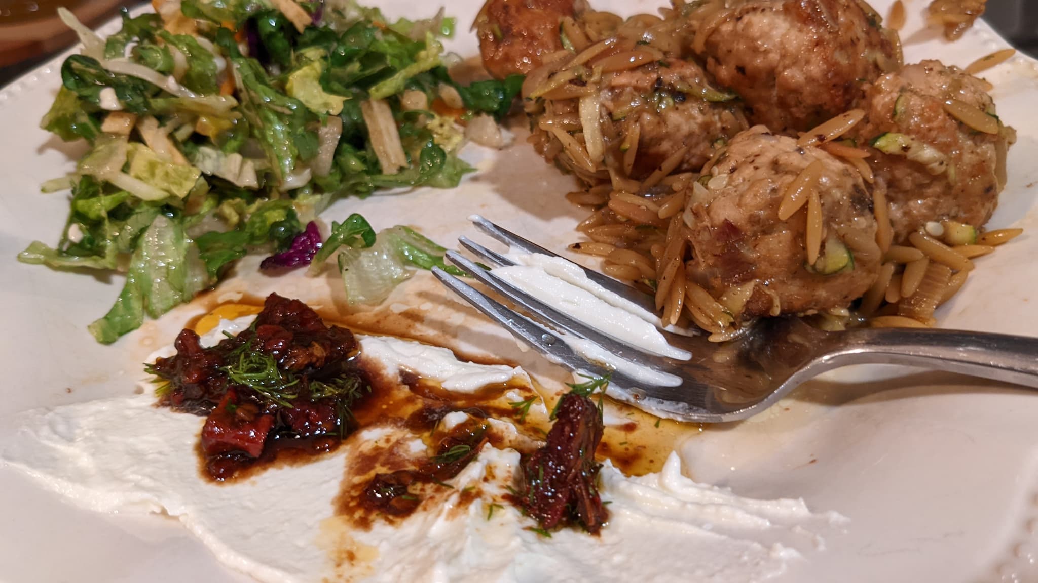 Glazed meatballs and orzo pasta next to greens and a white spread with balsamic tomato dressing