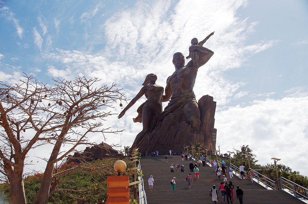 large monument of a woman and a man holding a small child with people on steps leading up to the monument