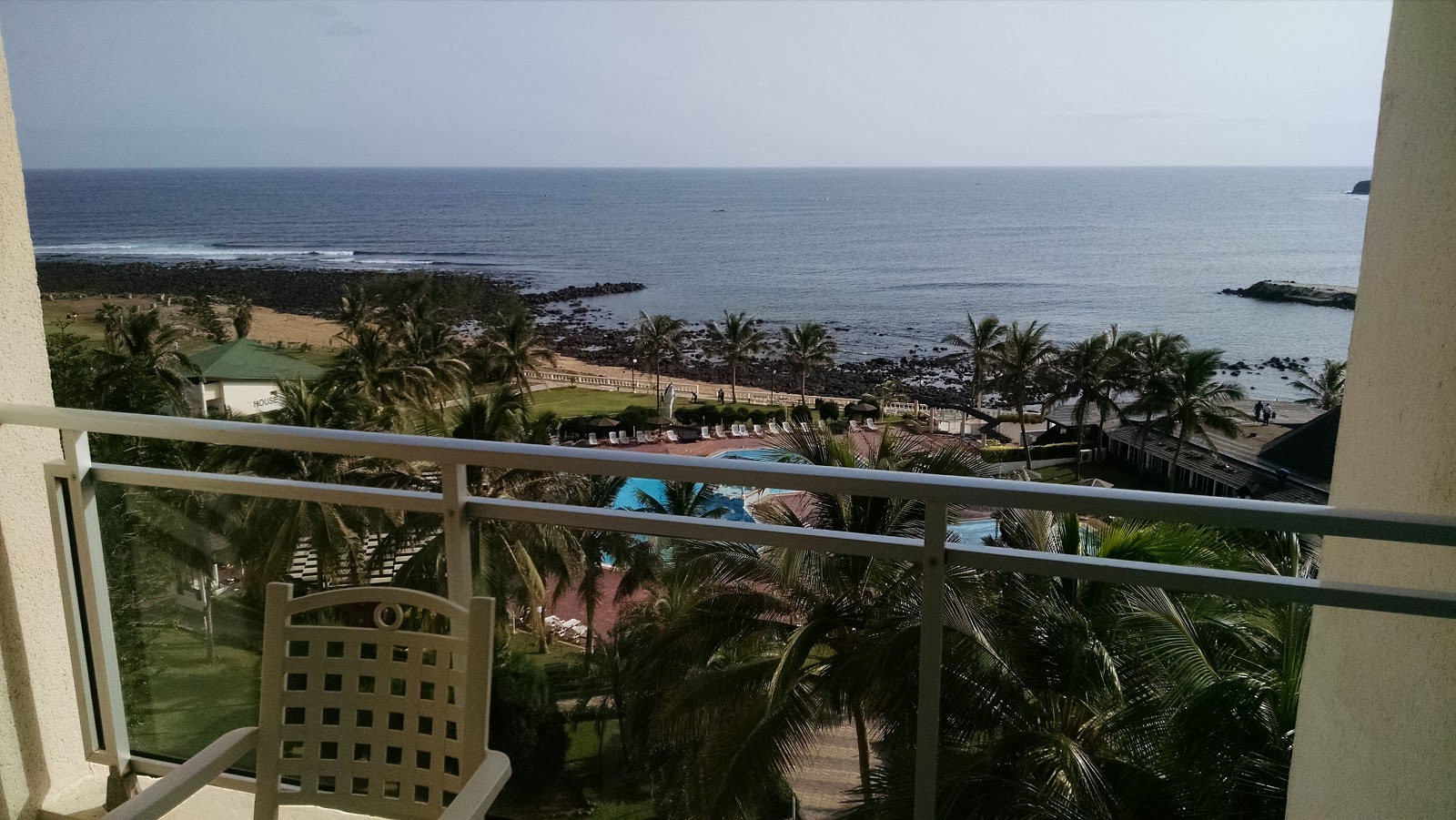 View of the ocean and a pool surrounded by palm trees from a hotel balcony