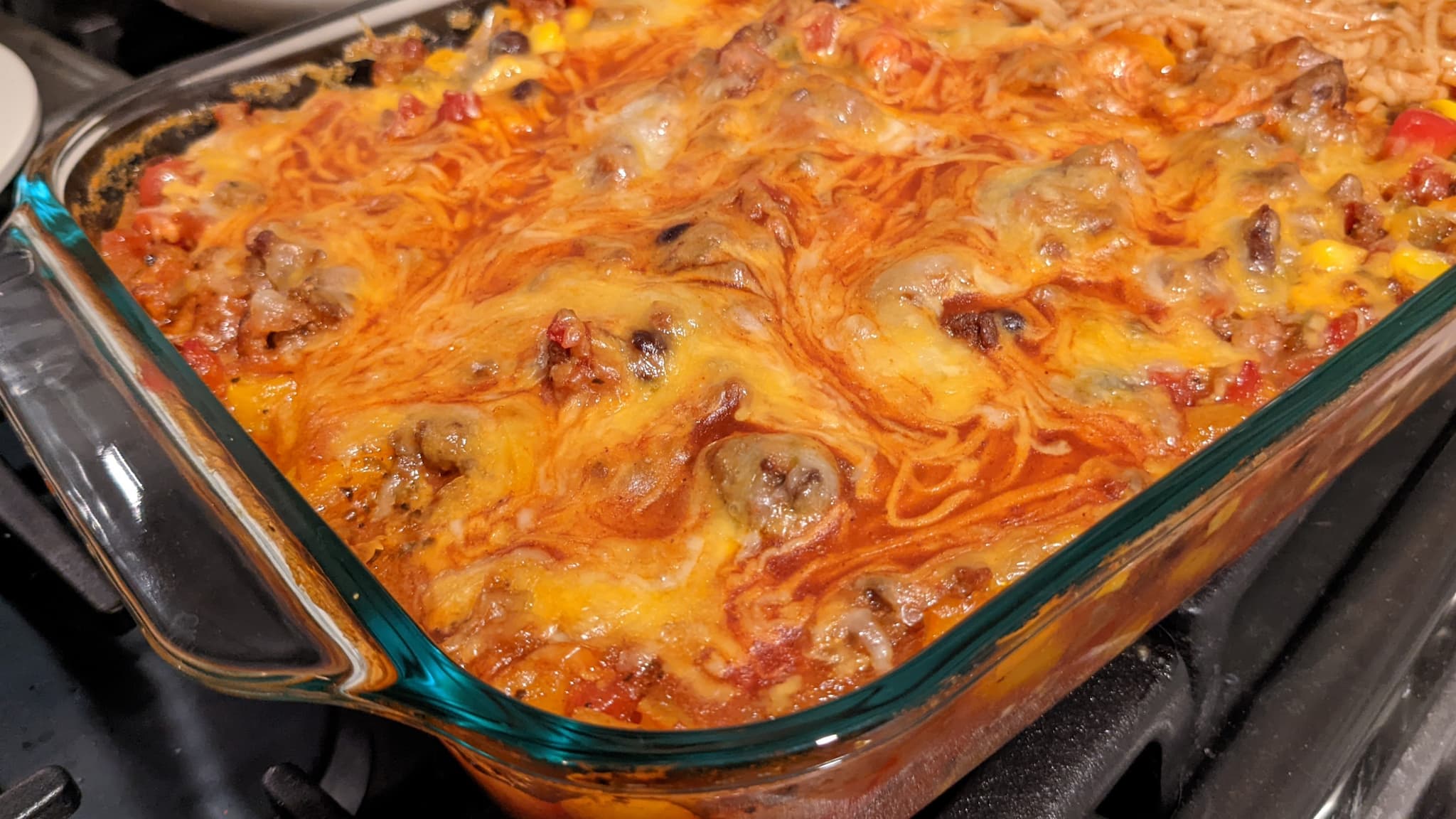 Glass casserole dish with cheesy top on ground beef and sauce.